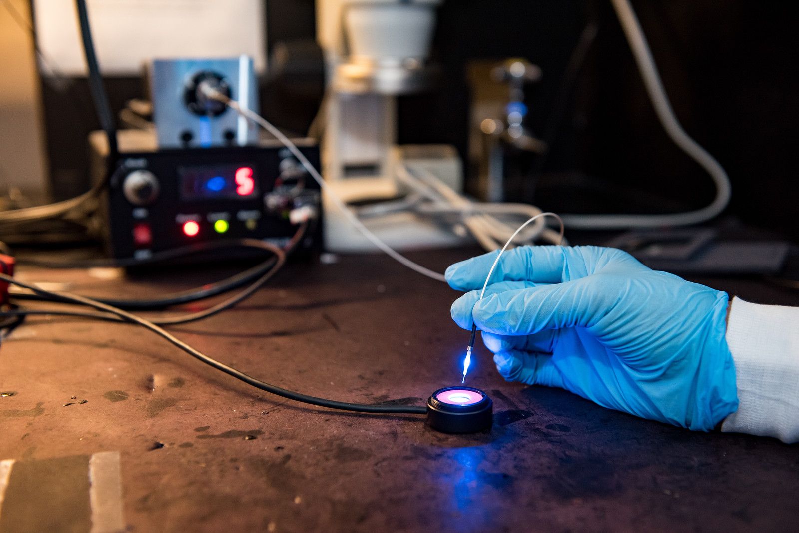 a gloved hand working with a lighted piece of scientific equipment