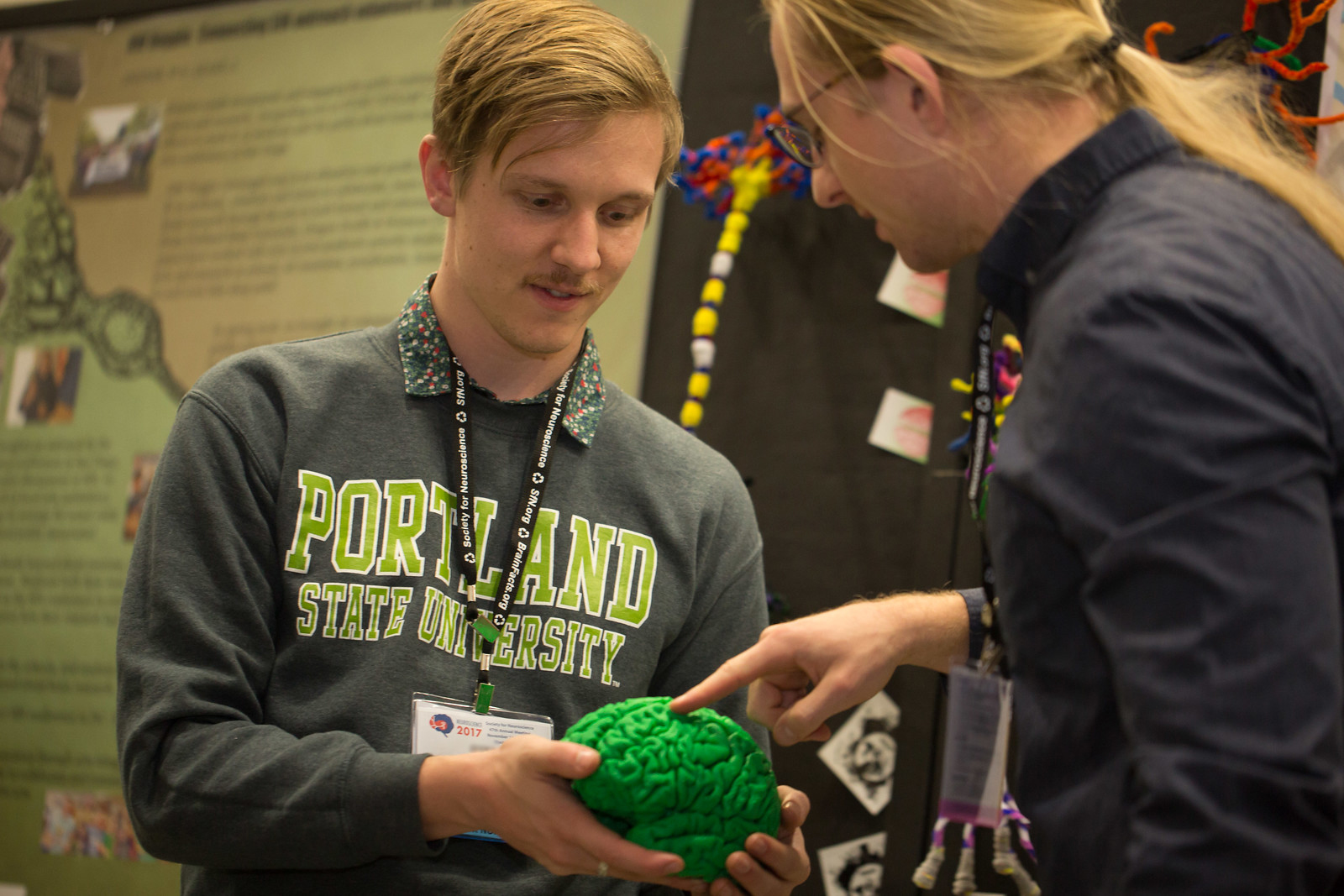 a person holding out a scientific brain model as another person touches the model